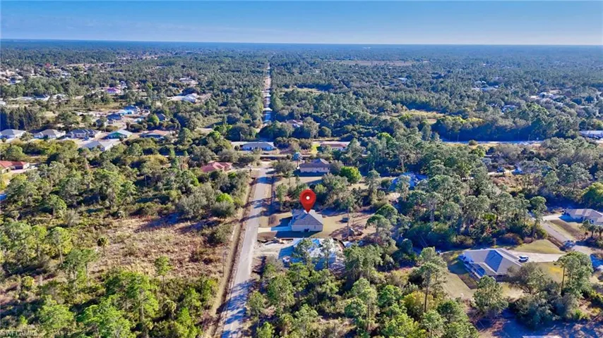 Aerial view of property and surrounding area featuring a heavily wooded area and nearby suburban area