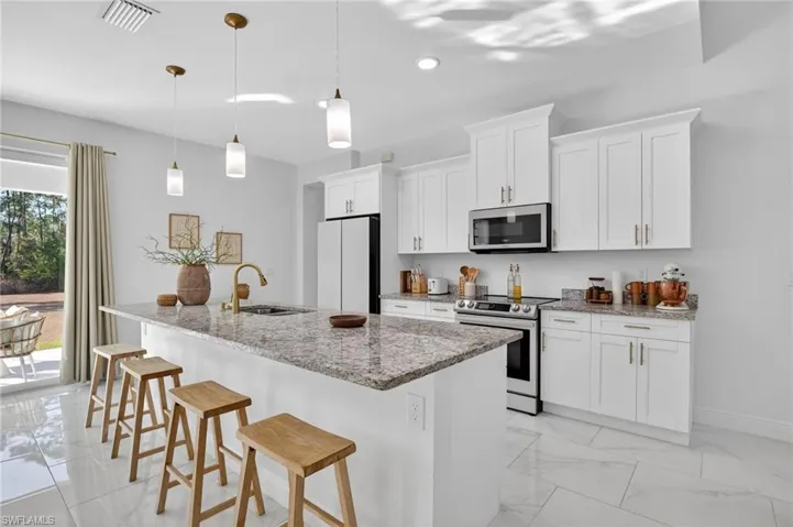 Kitchen with a breakfast bar area, stainless steel appliances, light stone counters, a kitchen island with sink, and white cabinets