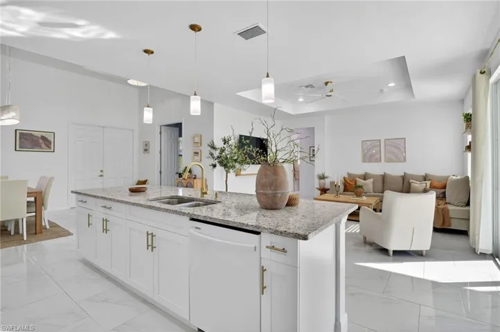 Kitchen featuring a raised ceiling, white cabinetry, light stone counters, white dishwasher, and pendant lighting
