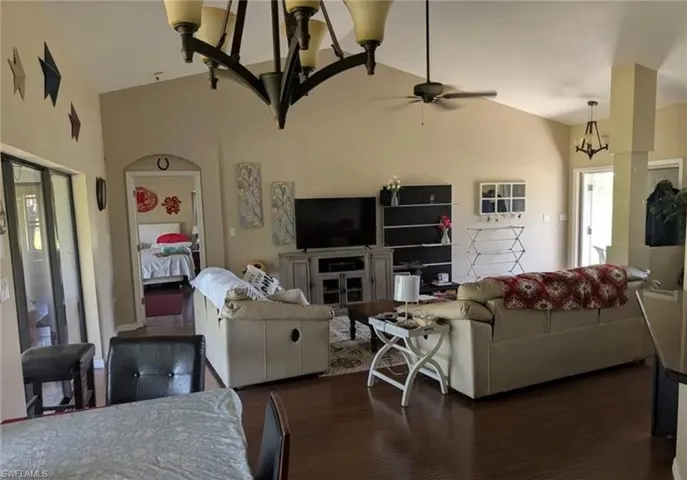 Living room with a chandelier, vaulted ceiling, wood finished floors, and a ceiling fan