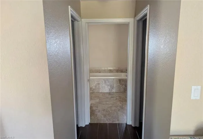 Hallway with a textured wall and dark wood-type flooring