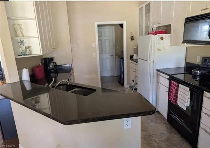 Kitchen featuring black appliances, dark countertops, white cabinets, glass insert cabinets, and a peninsula