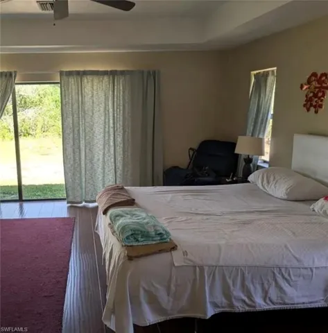 Bedroom featuring multiple windows, wood finished floors, access to exterior, and a ceiling fan