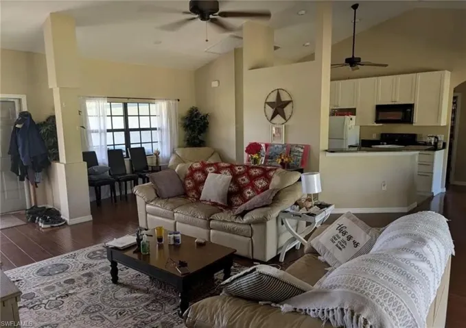 Living room with a ceiling fan, dark wood-type flooring, and high vaulted ceiling