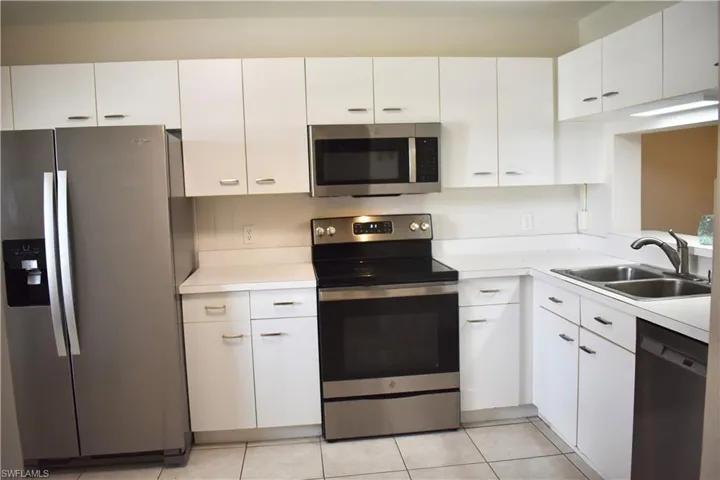 Kitchen with light tile, large sink, white cabinets, and appliances with stainless steel finishes