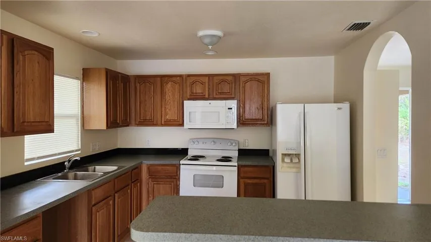Kitchen featuring healthy amount of natural light, white appliances, arched walkways, and wood finish cabinetry