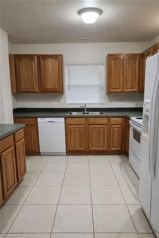 Kitchen featuring wood finish cabinets, dark countertops, white appliances, a textured ceiling, and light tile patterned floors