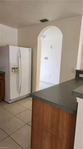 Kitchen featuring dark countertops, white fridge, light tile patterned floors, arched walkways, and a peninsula