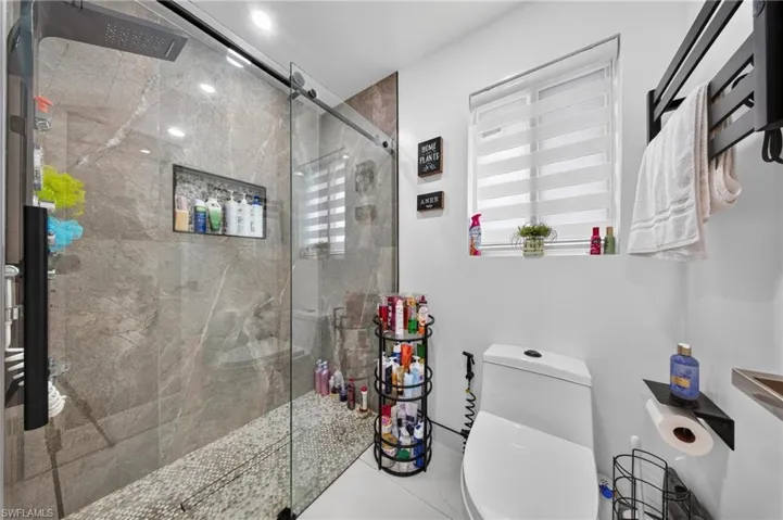 Glass-enclosed shower with stone-finish wall tile, pebble-style flooring, and a built-in shower niche
