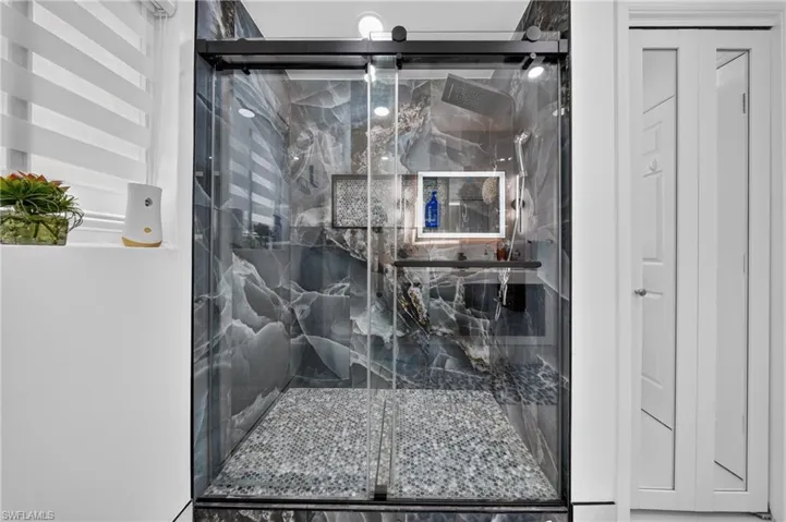 Glass-enclosed shower with dark-toned, veined wall panels and a pebble-finish floor