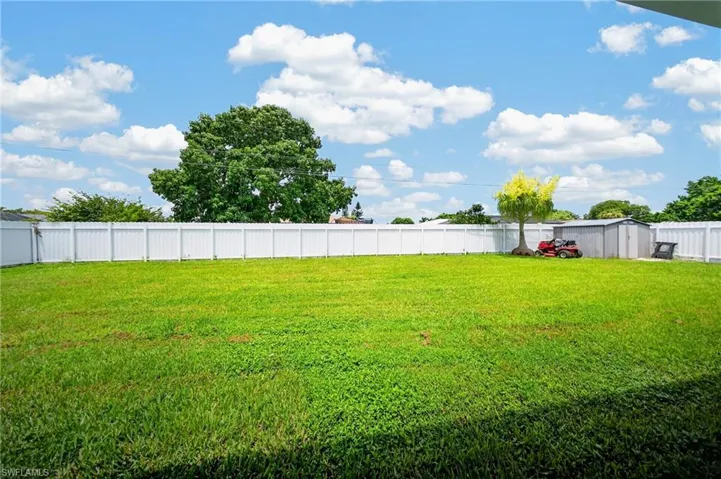 Expansive lawn area featuring a full perimeter white privacy fence, mature trees, and a metal storage shed