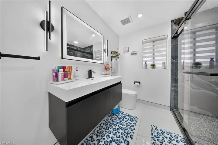 Floating vanity with integrated sink, black framed mirror, walk-in shower with glass enclosure, tiled shower walls, and white tiled flooring