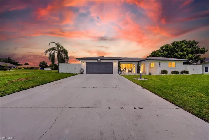 Expansive concrete driveway, attached two-car garage, white exterior finish, arched entryway, and a manicured front lawn