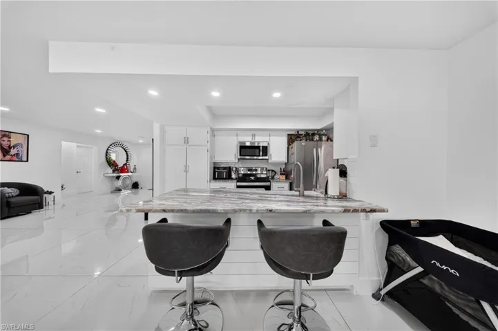 Modern kitchen island with a stone-finish countertop, white shaker-style cabinetry, stainless steel appliances, and white tile flooring
