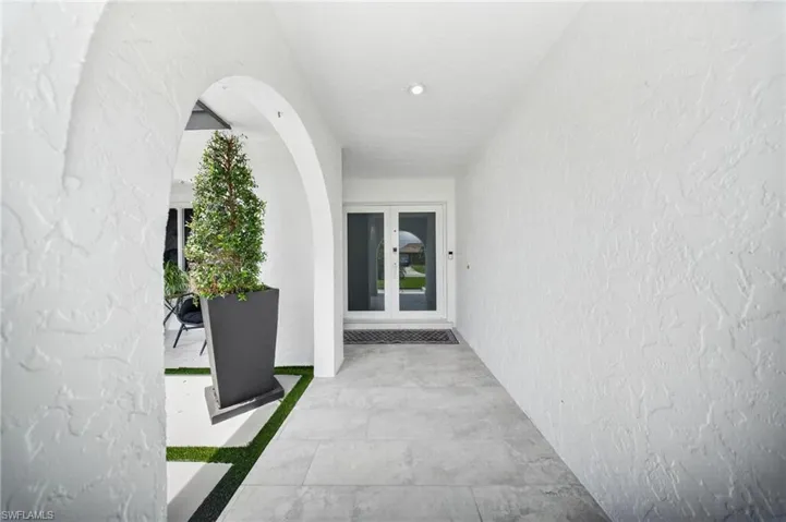 Arched entryway with a textured white stucco finish, recessed lighting, and light-toned tile flooring