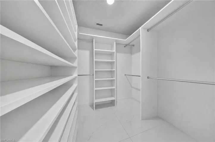Walk-in closet with extensive built-in shelving, multiple hanging rods, corner shelving unit, and tile flooring