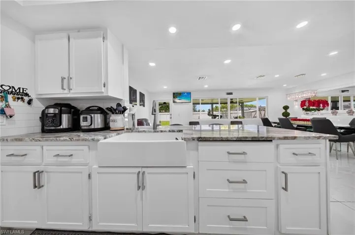 White shaker cabinetry with modern hardware, farmhouse sink, integrated lighting, and granite-style countertops