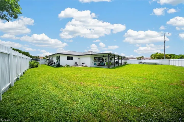 Expansive green lawn, white perimeter fencing, and a covered patio area