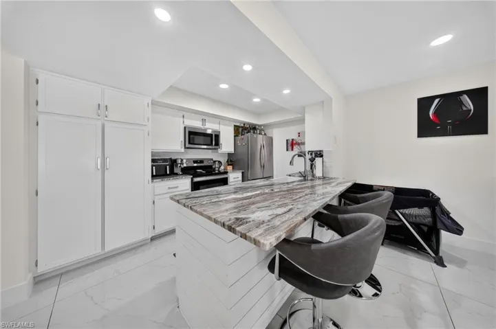 Kitchen featuring a multi-tone island countertop, stainless steel appliances, white cabinetry, and recessed lighting