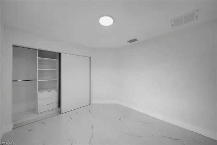 Spacious room featuring wood-finish flooring, a contemporary ceiling light fixture, and a built-in closet system with sliding doors, shelving, and drawers