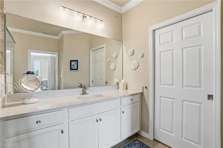 Spacious primary bath featuring crown molding, two vanities, large glass-enclosed shower, patterned tile floors, and a linen closet.