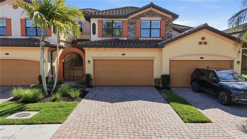 Coach home condo 2nd floor, featuring stone & stucco siding, entry gate, and decorative driveway