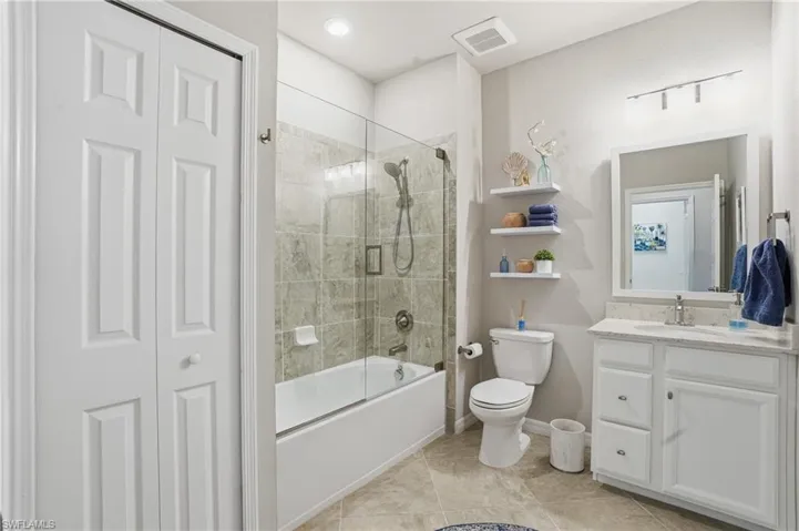 Elegant bathroom with quartz counters, white cabinets, modern mirror, designer lighting, and a bath/shower combo with glass door.