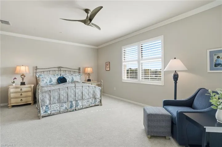 Inviting primary bedroom retreat with warm morning light, crown molding, plantation shutters, and lanai sliders with designer drapes.