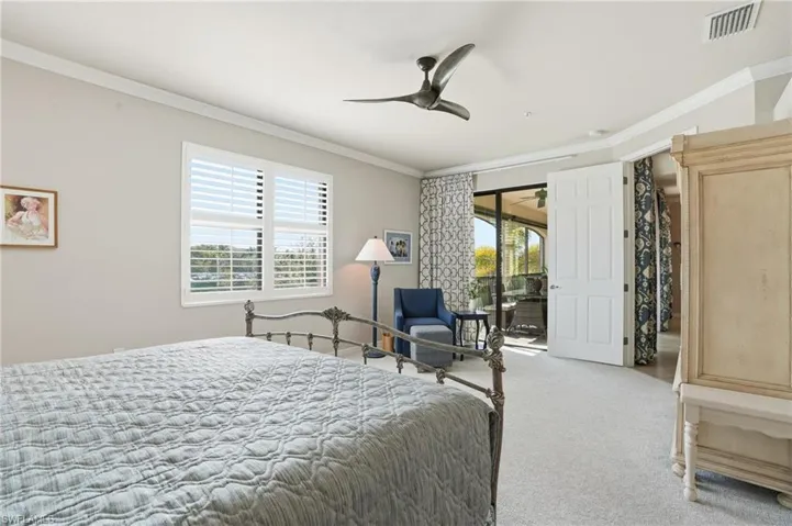 Sun-filled primary bedroom with crown molding, plantation shutters, designer-draped lanai sliders, and a comfortable sitting area to relax.