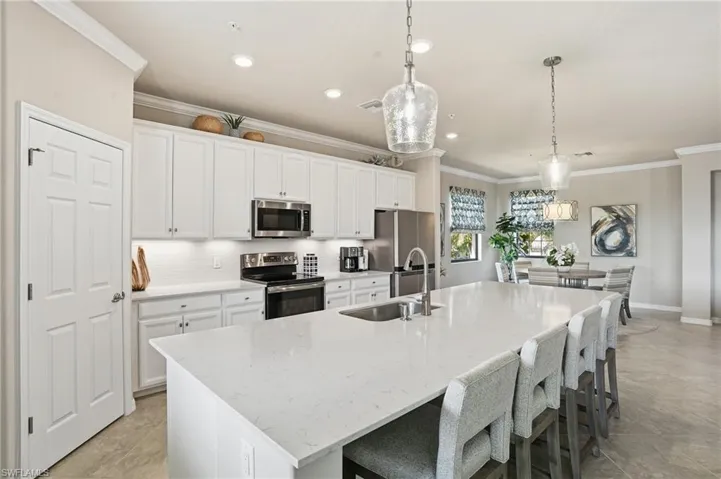Spacious open kitchen featuring white cabinets, quartz counters, a designer backsplash, and a large entertaining island seamlessly connected to the dining area.