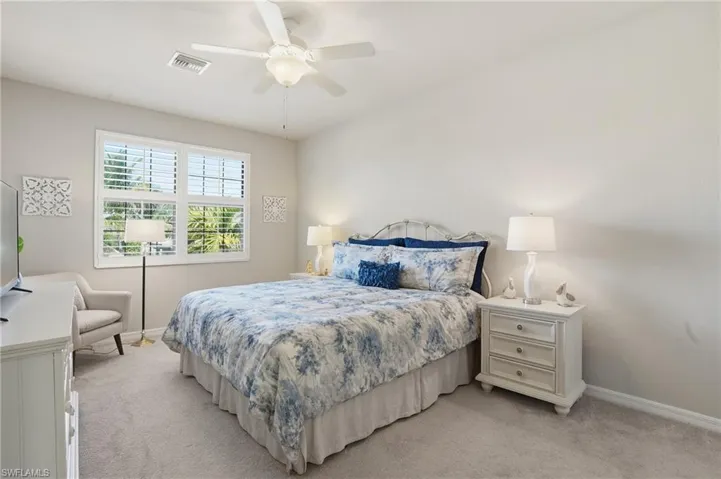 Spacious, light-filled guest bedroom with neutral tones, room to sit, and plantation shutters.