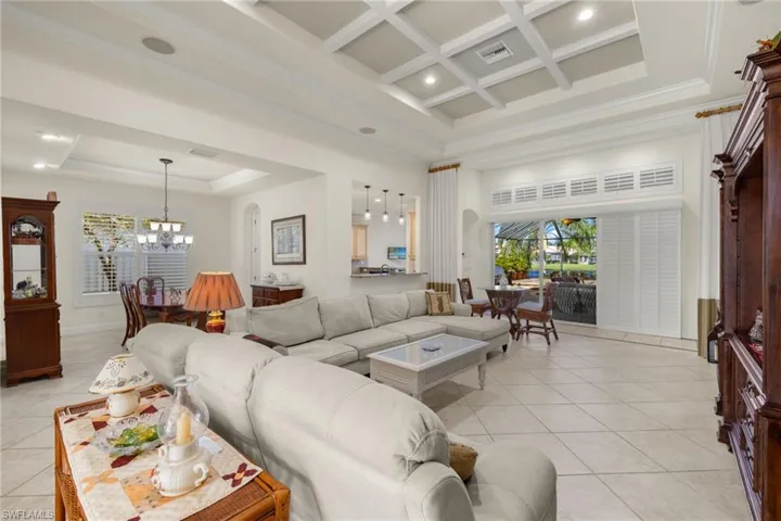 Tiled living room with a tray ceiling, an inviting chandelier, beam ceiling, coffered ceiling, and a towering ceiling