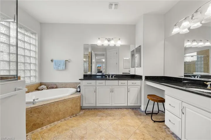 Bathroom featuring dual vanity, a healthy amount of sunlight, tile patterned flooring, and a relaxing tiled tub