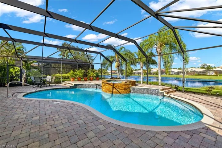 View of swimming pool featuring a patio area, pool water feature, an in ground hot tub, a water view, and glass enclosure