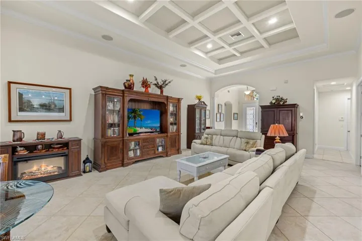 Living room with light tile patterned floors, a high ceiling, crown molding, beam ceiling, and coffered ceiling