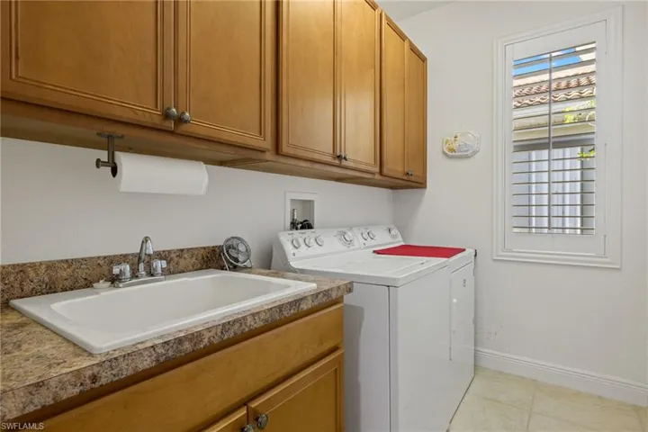 Laundry room featuring washing machine and clothes dryer, sink, light tile patterned flooring, and cabinets