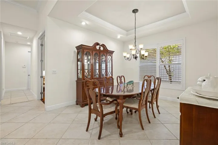 Dining area featuring ornamental molding, a tray ceiling, a notable chandelier, and light tile patterned floors