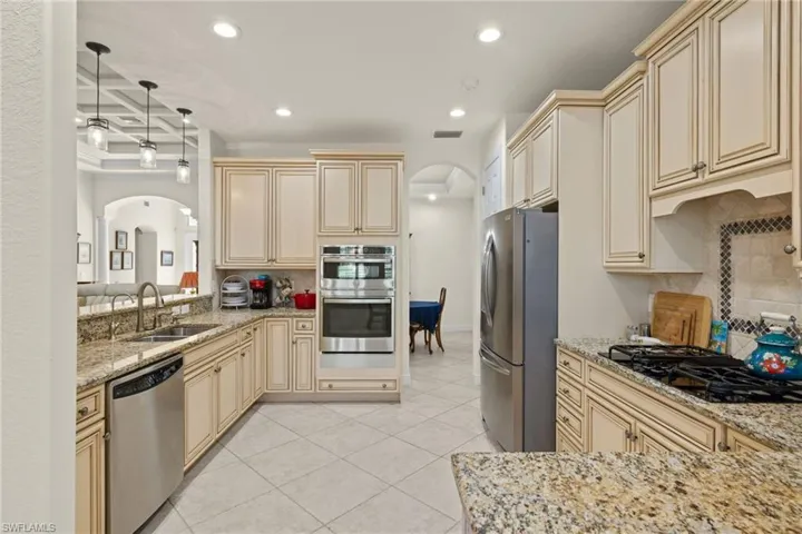 Kitchen with light tile patterned flooring, cream cabinetry, stainless steel appliances, decorative backsplash, and sink