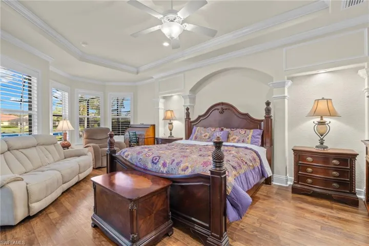 Bedroom with crown molding, decorative columns, a tray ceiling, ceiling fan, and hardwood / wood-style flooring