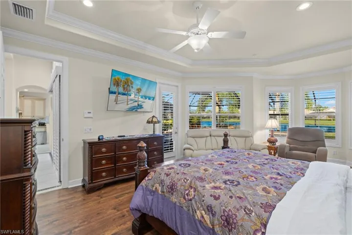 Bedroom featuring ceiling fan, multiple windows, dark hardwood / wood-style floors, and a tray ceiling