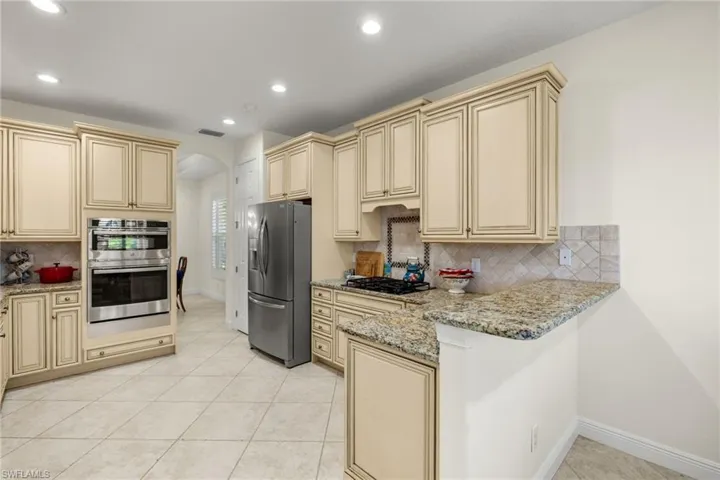 Kitchen featuring light tile patterned flooring, stainless steel appliances, decorative backsplash, light stone countertops, and kitchen peninsula