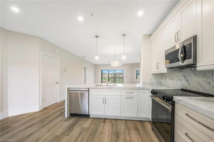 Kitchen with white cabinetry, hanging light fixtures, light hardwood / wood-style floors, kitchen peninsula, and stainless steel appliances