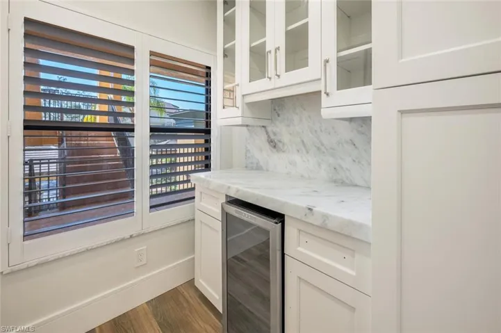 Kitchen with white cabinetry, beverage cooler, backsplash, light stone countertops, and dark wood-type flooring