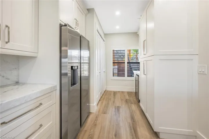 Kitchen with stainless steel fridge, light stone countertops, light wood-type flooring, and white cabinets