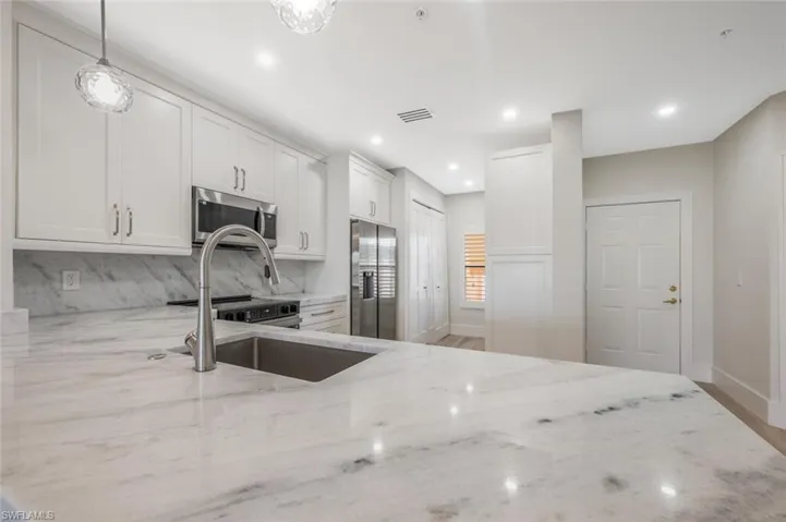 Kitchen featuring appliances with stainless steel finishes, backsplash, white cabinets, hanging light fixtures, and light stone counters