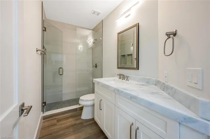 Bathroom featuring wood-type flooring, a shower with shower door, vanity, and toilet