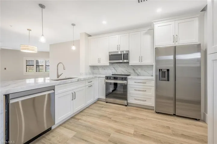 Kitchen with decorative light fixtures, sink, white cabinets, light stone counters, and stainless steel appliances