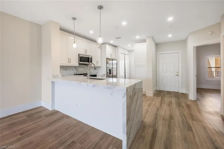 Kitchen with white cabinetry, decorative backsplash, hanging light fixtures, kitchen peninsula, and stainless steel appliances