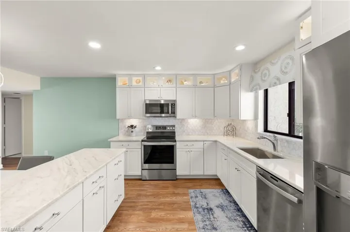 Kitchen featuring light wood-style flooring, a sink, appliances with stainless steel finishes, white cabinetry, and backsplash