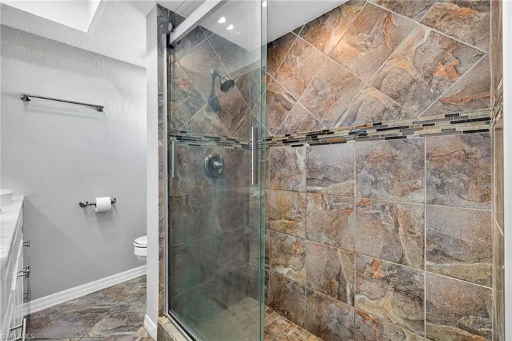 Full bath featuring vanity, a tile shower, and a textured wall